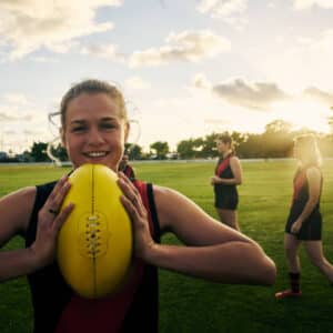 Shot of a young woman holding a football on a field with her team in the background